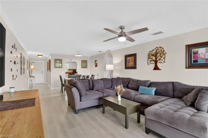 Open-concept living area featuring light wood-finish flooring, a contemporary ceiling fan with integrated lighting, and crown molding