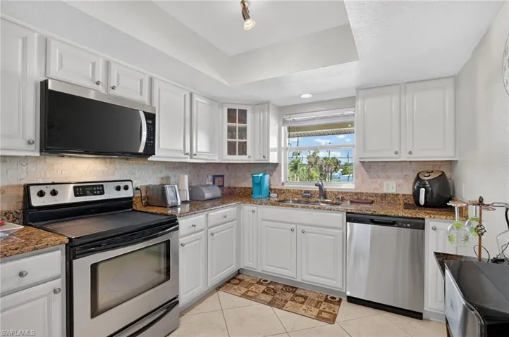 Kitchen featuring white cabinetry, granite-style countertops, stainless steel appliances, and a tiled backsplash