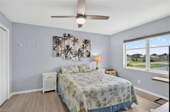 Bedroom featuring wood-finish flooring, a ceiling fan with integrated lighting, and a window offering a waterside perspective