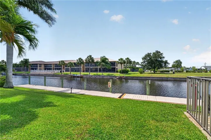 Waterfront property featuring a private boat dock, lush green lawn, mature palm trees, and canal access