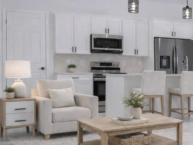 Kitchen with stainless steel appliances, white cabinets, backsplash, light stone counters, and a kitchen breakfast bar
