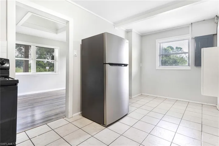 Kitchen featuring black electric range oven, light tile patterned floors, stainless steel fridge, and a wealth of natural light