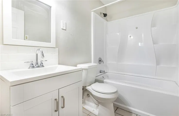 Full bathroom with vanity, tile patterned floors, tasteful backsplash, shower / bath combination, and toilet