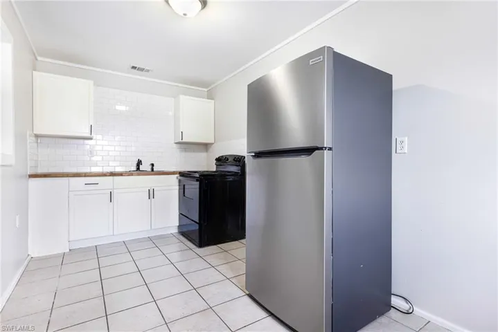 Kitchen featuring white cabinetry, tasteful backsplash, stainless steel fridge, black / electric stove, and light tile patterned floors