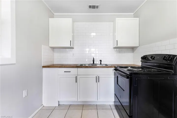Kitchen featuring black / electric stove, light tile patterned floors, wooden counters, and white cabinets