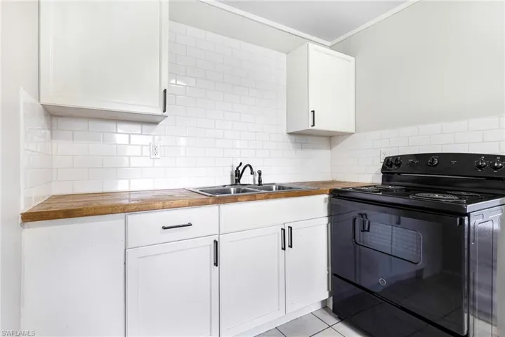 Kitchen with sink, black electric range oven, decorative backsplash, light tile patterned flooring, and white cabinetry