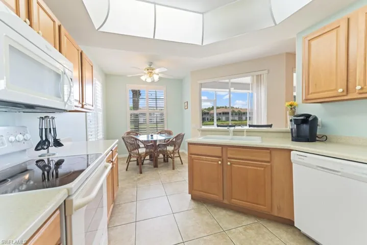 Kitchen featuring ceiling fan, sink, white appliances, and light tile floors
