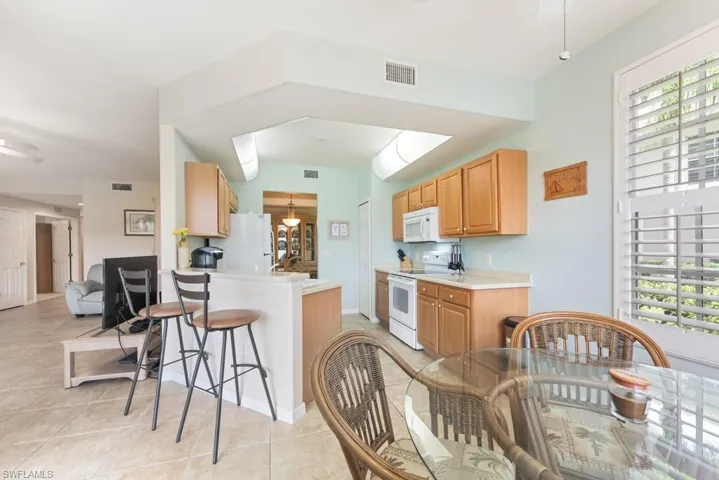 Kitchen with white appliances, plenty of natural light, light tile floors, and a kitchen bar
