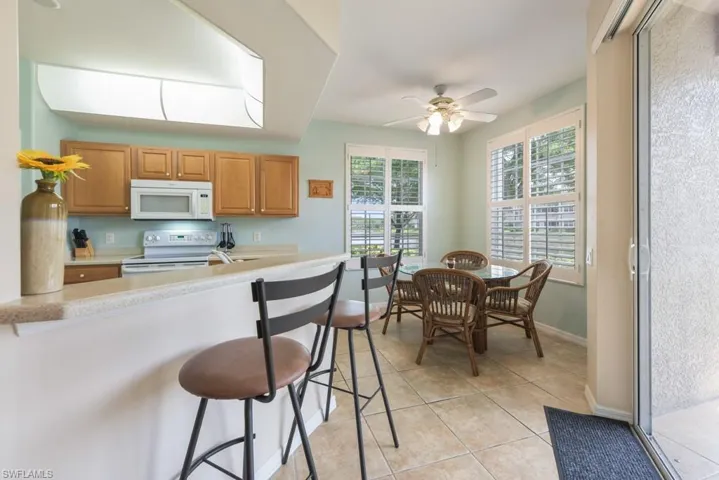 Kitchen featuring ceiling fan, a breakfast bar, light tile flooring, and white appliances