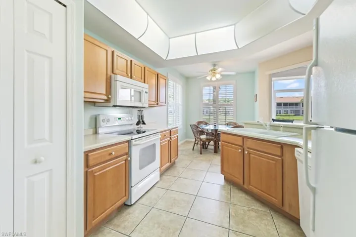 Kitchen with white appliances, sink, ceiling fan, and light tile floors