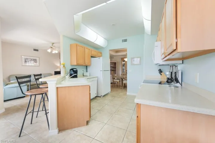 Kitchen with light tile flooring, ceiling fan, a breakfast bar area, sink, and white appliances