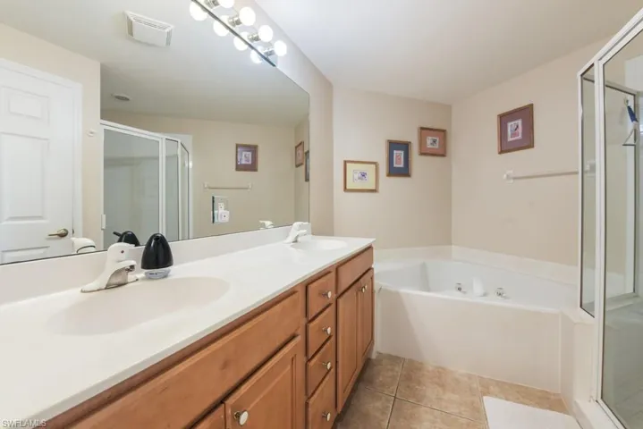 Bathroom with vanity with extensive cabinet space, separate shower and tub, dual sinks, and tile floors