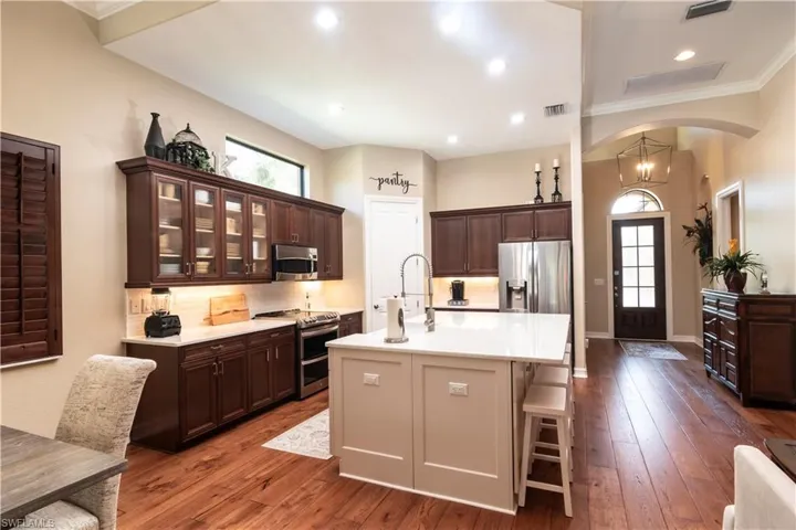 Kitchen with stainless steel appliances, a center island with sink, hardwood / wood-style floors, decorative backsplash, and ornamental molding