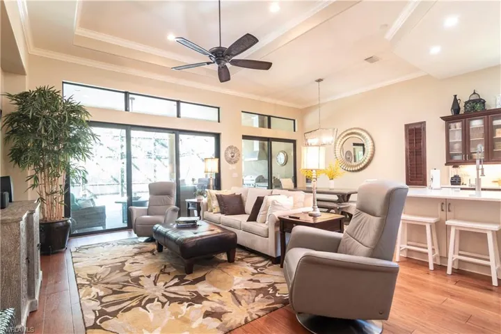 Living room with ornamental molding, light wood-type flooring, ceiling fan with notable chandelier, and a tray ceiling