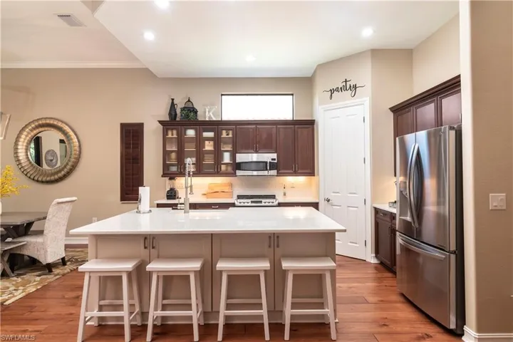 Kitchen featuring a breakfast bar, appliances with stainless steel finishes, ornamental molding, an island with sink, and wood flooring