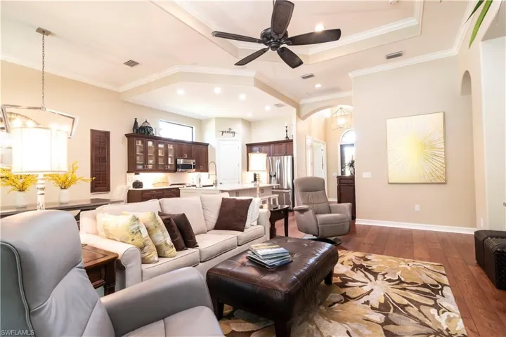 Living room featuring ceiling fan with notable chandelier, dark hardwood / wood-style floors, and crown molding