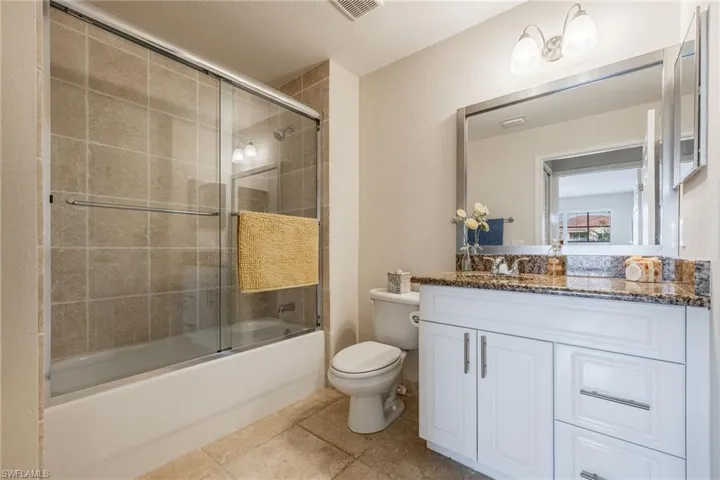 Downstairs full bathroom featuring bath / shower combo with glass door, toilet, vanity, and tile patterned flooring