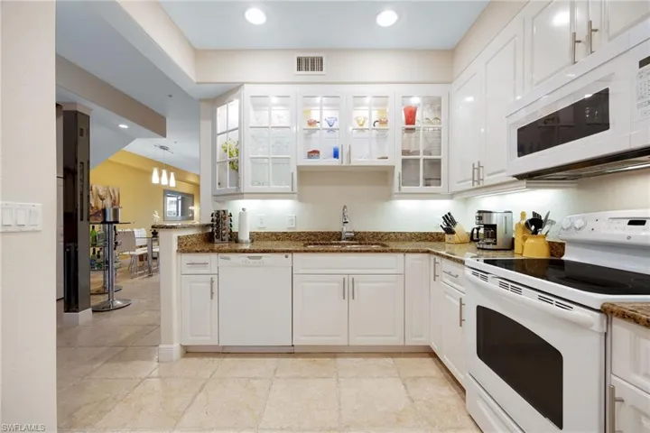 Kitchen with white appliances, white cabinetry, sink, granite countertops, and kitchen peninsula