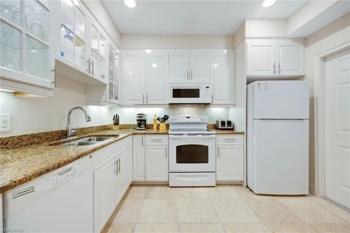 Kitchen with granite counters, sink, white appliances, and white cabinets