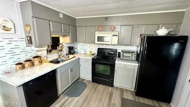 Kitchen featuring gray cabinets, sink, black appliances, crown molding, and light wood-type flooring