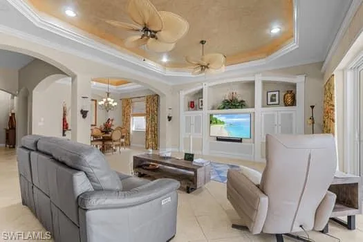 Tiled living room with ornamental molding, a tray ceiling, and ceiling fan with notable chandelier