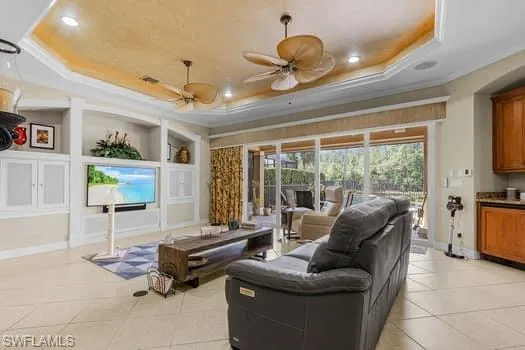 Living room featuring ceiling fan, a tray ceiling, and light tile patterned floors