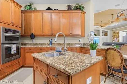 Kitchen with a center island with sink, light stone countertops, light tile patterned flooring, sink, and stainless steel double oven