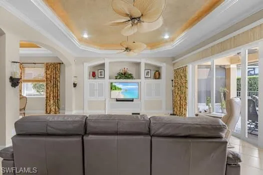 Living room featuring ornamental molding, tile patterned floors, a tray ceiling, and ceiling fan
