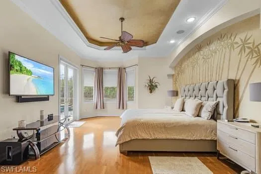 Bedroom with access to exterior, a raised ceiling, wood-type flooring, and ceiling fan