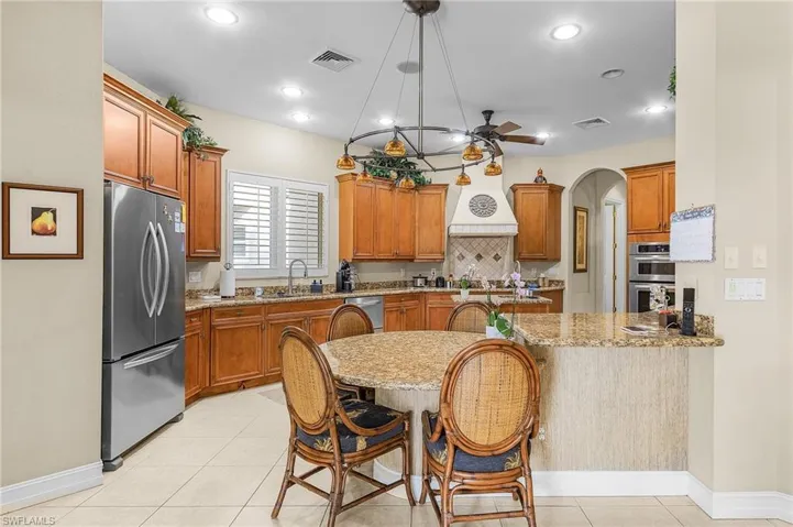 Kitchen featuring a kitchen breakfast bar, light stone countertops, pendant lighting, appliances with stainless steel finishes, and ceiling fan with notable chandelier