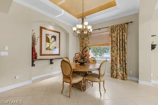 Dining space with a raised ceiling, light tile patterned floors, and a chandelier