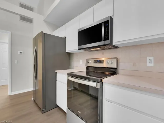 Kitchen featuring light hardwood / wood-style flooring, tasteful backsplash, white cabinetry, and appliances with stainless steel finishes