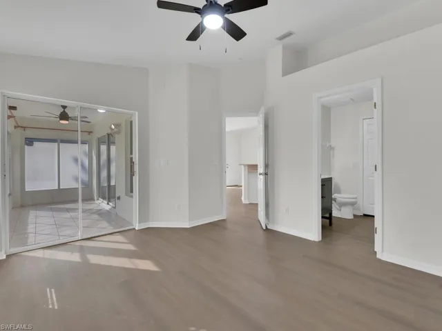 Unfurnished bedroom with hardwood / wood-style floors, connected bathroom, ceiling fan, and lofted ceiling