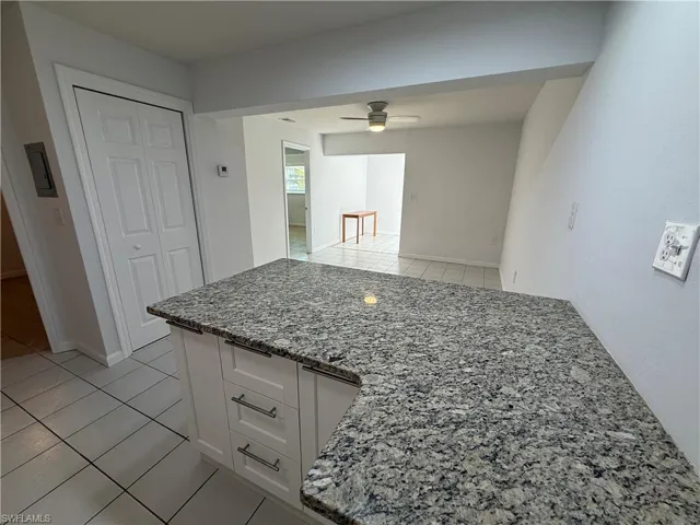 Kitchen with light tile patterned floors, white cabinets, a peninsula, light stone countertops, and ceiling fan