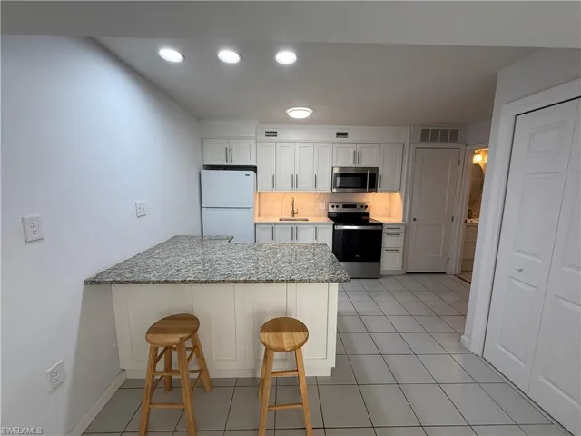Kitchen with appliances with stainless steel finishes, white cabinetry, a peninsula, a breakfast bar area, and light stone counters
