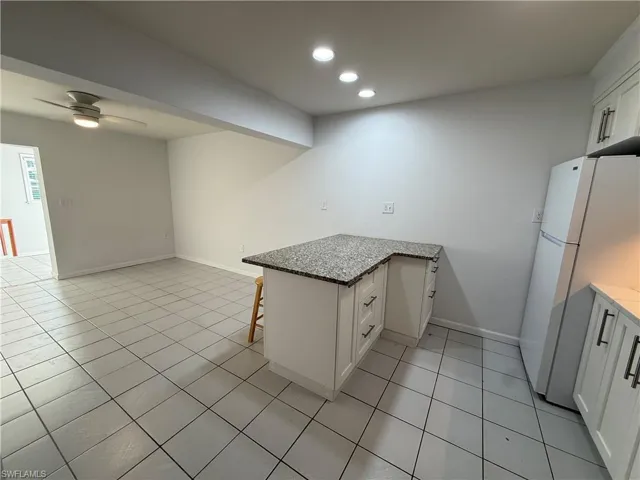 Kitchen with a peninsula, a breakfast bar area, freestanding refrigerator, white cabinets, and ceiling fan