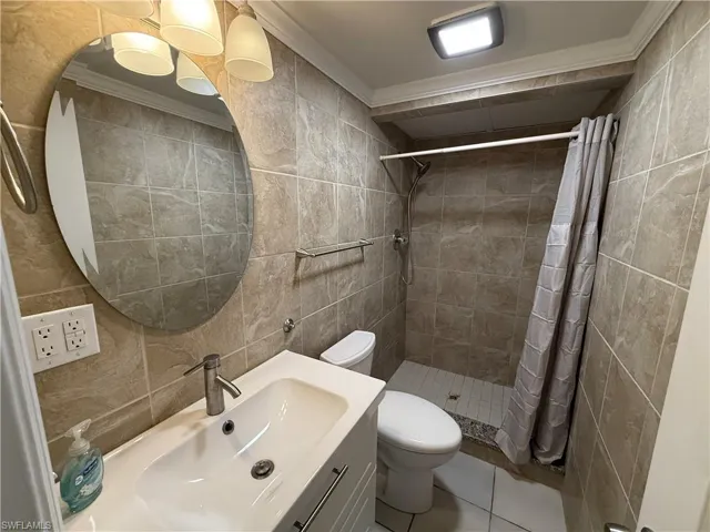 Full bathroom with tile walls, vanity, ornamental molding, a stall shower, and light tile patterned floors