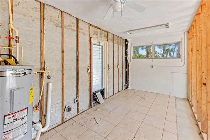 Basement with light tile flooring, electric water heater, wood walls, and ceiling fan