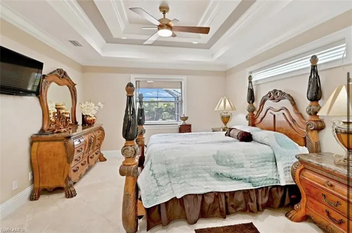 Bedroom with a tray ceiling, ornamental molding, light tile flooring, and ceiling fan