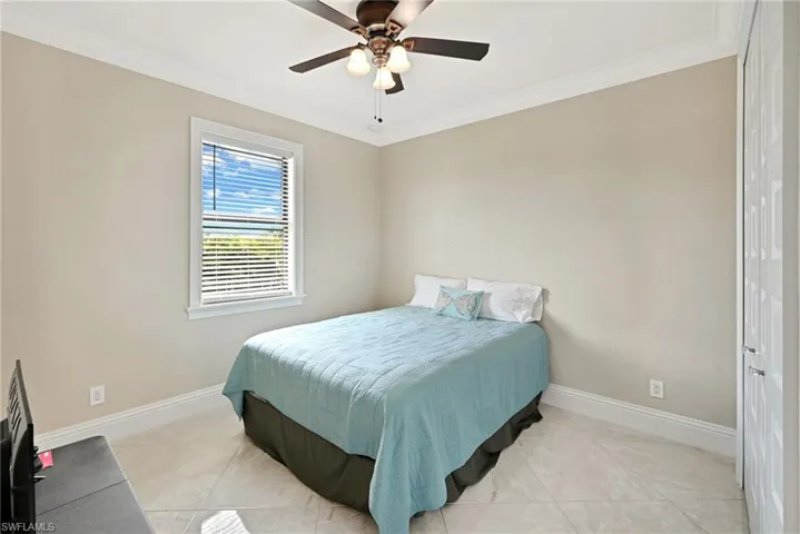 Bedroom with ceiling fan, light tile floors, and crown molding
