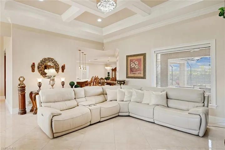 Living room with ornamental molding, coffered ceiling, light tile flooring, and a chandelier