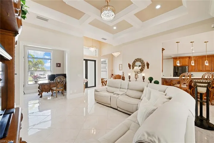 Living room featuring a notable chandelier, a towering ceiling, coffered ceiling, and light tile floors