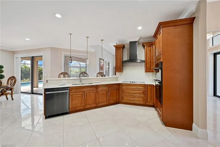 Kitchen featuring decorative light fixtures, kitchen peninsula, wall chimney exhaust hood, stainless steel dishwasher, and sink