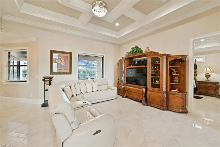 Tiled living room featuring coffered ceiling, ornamental molding, and a notable chandelier