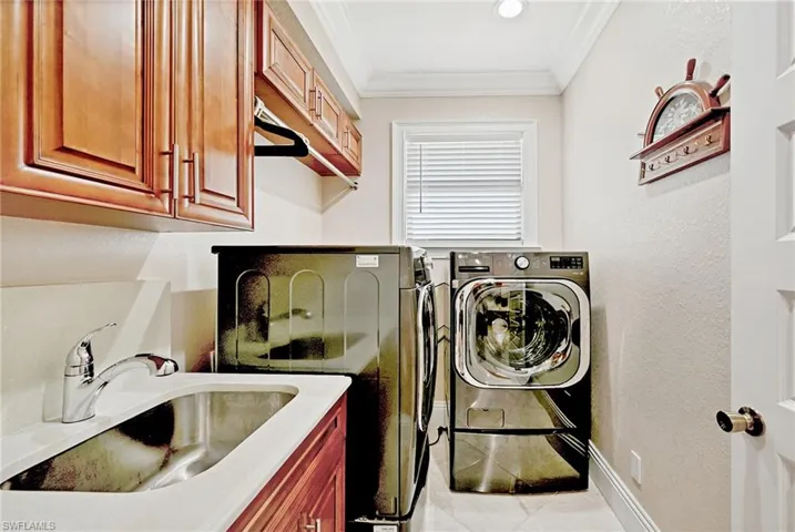 Clothes washing area with crown molding, light tile flooring, sink, washer and clothes dryer, and cabinets