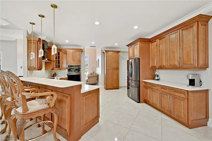 Kitchen featuring wall chimney range hood, appliances with stainless steel finishes, kitchen peninsula, pendant lighting, and light tile floors