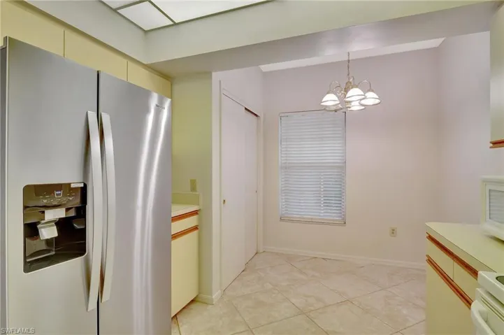 Kitchen with range, light tile patterned floors, an inviting chandelier, hanging light fixtures, and stainless steel refrigerator with ice dispenser