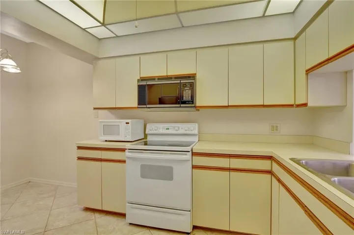 Kitchen featuring cream cabinetry, white appliances, and light tile patterned floors