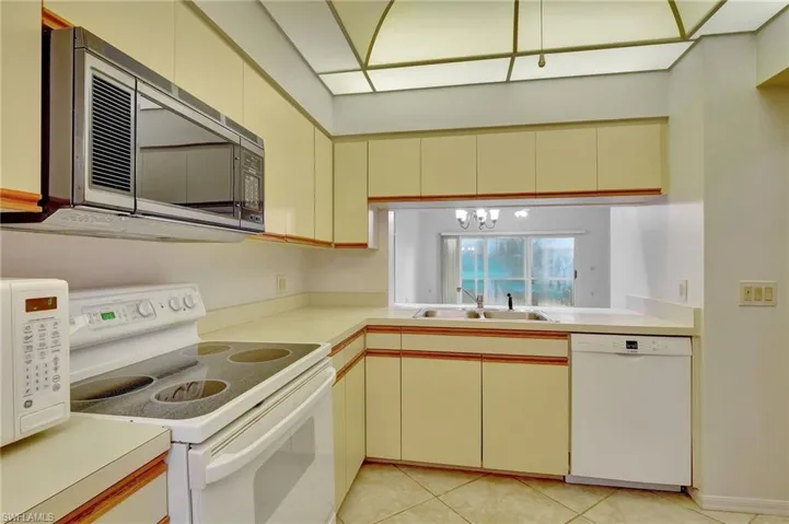 Kitchen featuring light tile patterned flooring, sink, white appliances, and cream cabinetry