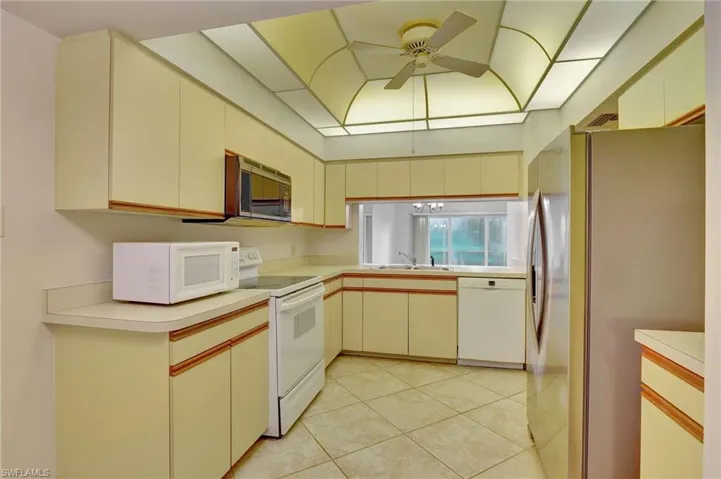 Kitchen with cream cabinets, ceiling fan, white appliances, sink, and light tile patterned floors